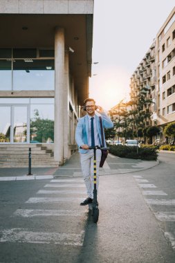 Genç modern bir adam şehirde elektrikli scooter kullanıyor ve kullanıyor ve müzik dinliyor. Modern ve ekolojik ulaşım kavramı.