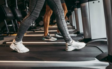 Modern spor salonunda koşu bandında koşan genç, zinde bir kadın ve erkek. Hareket eden bacaklara yakın çekim.