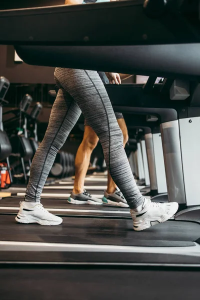 Modern spor salonunda koşu bandında koşan genç, zinde bir kadın ve erkek. Hareket eden bacaklara yakın çekim.