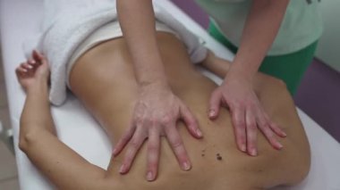 Beautiful young adult brunette receiving professional relaxation massage treatment at beauty spa salon.