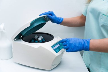 Mavi eldiven giyen laboratuvar teknisyeni içinde numuneler bulunan modern bir santrifüj işletiyor. Klinik bir ortamda tıbbi analize hazırlanıyor.