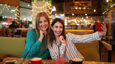 İki bayan arkadaş bir restoranda bir masada oturmuş, içki içip, akıllı bir telefonla selfie çekiyorlar, çeşitli neşeli ve komik ifadeler takınıyorlar.