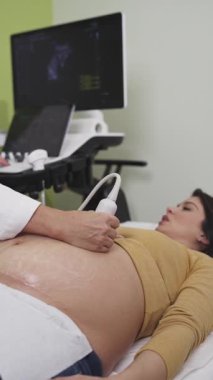 Female doctor doing ultrasound scan for a beautiful pregnant woman. Side view. Modern pregnancy and healthcare concept.