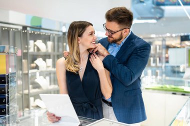 Happy couple engaging in retail therapy, man gifting woman a heart pendant necklace at a luxury jewelry store, celebrating a special occasion or anniversary