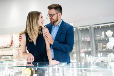 Happy couple engaging in retail therapy, man gifting woman a heart pendant necklace at a luxury jewelry store, celebrating a special occasion or anniversary