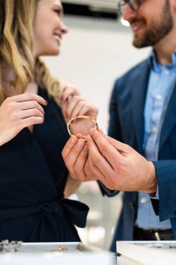 Young couple admires a delicate bracelet in a luxury jewelry boutique, shopping for a special gift and sharing an intimate, elegant moment of celebration and romance
