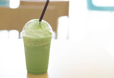 Closeup plastik bardak buz matcha frappe kapıdan, seçici odak gelen ışık üzerinde ahşap tablo