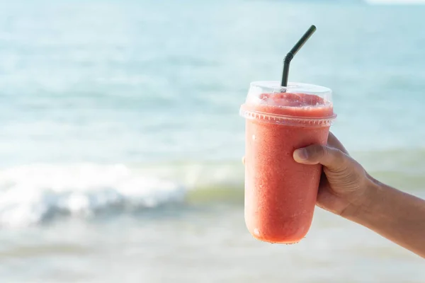 Mão segurando vidro de smoothie de morango com fundo de água do mar, férias e tempo de relaxamento — Fotografia de Stock
