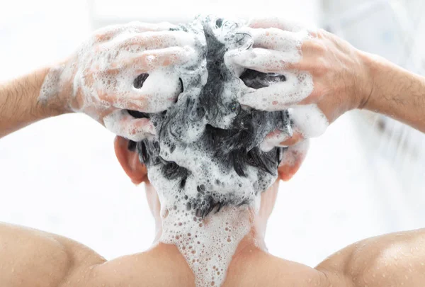 Vértes fiatalember mosás haját samponnal a fürdőszoba egészségügyi koncepció, szelektív összpontosít — Stock Fotó