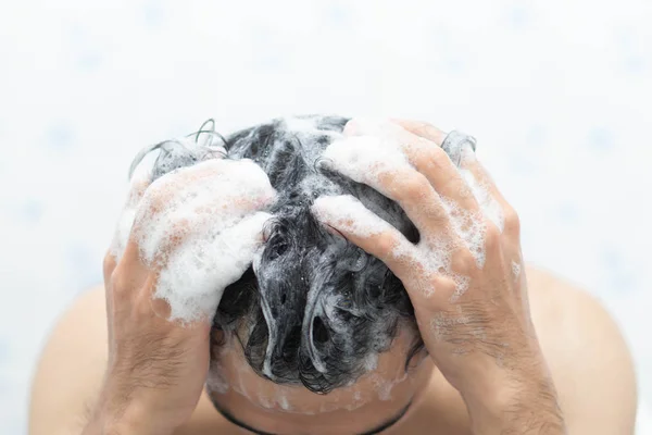 Closeup young man washing hair with with shampoo in the bathroom, health care concept, selective focus