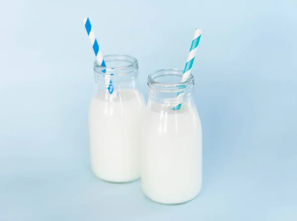 Butelka świeżego mleka ze słomką na jasnoniebieskim tle, zdrowa koncepcja żywności — Zdjęcie stockowe