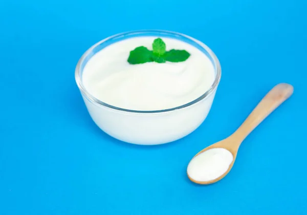 Close up yoghurt in glazen schaal met houten lepel op blauwe ondergrond — Stockfoto