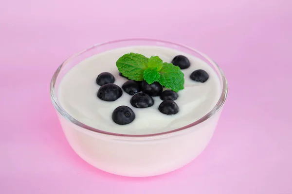 Nahaufnahme Joghurt mit frischen Blaubeeren in Glasschale auf rosa Hintergrund — Stockfoto