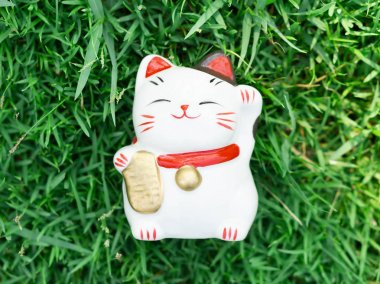 Maneki neko sabah güneş ışığıyla yeşil çimlerde, odaklan