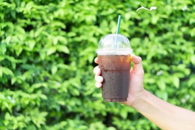 Kapalı kapılar ardında yeşil yapraklı bir bardak buzlu Americano kahvesi, seçici bir odak noktası.  