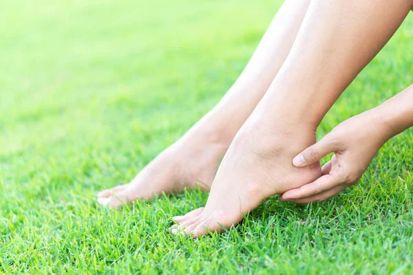 Женщина держит ногу с болью на зеленом фоне травы, здравоохранение и медицинская концепция — стоковое фото