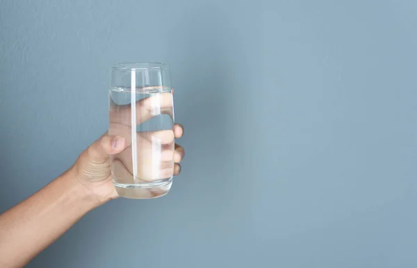Närbild kvinna hand hålla ett glas rent vatten för tusch med grå bakgrund, Sjukvård koncept — Stockfoto