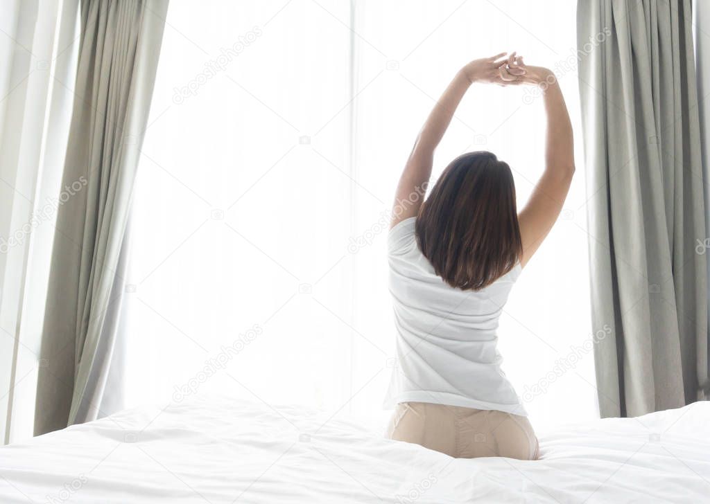 Close up woman sitting on the bed and stretching after waking up for relax in the morning with over light background