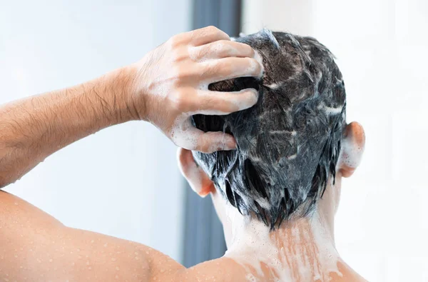 Closeup jovem homem lavar o cabelo com xampu no banheiro, conceito de cuidados de saúde, foco seletivo — Fotografia de Stock