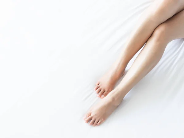 Nahaufnahme Frauenbeine auf weißem Bett mit überhellem Fenster, Schönheits- und Hautpflegekonzept, selektiver Fokus — Stockfoto