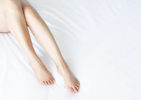 Primer plano piernas de la mujer en la cama blanca con sobre la ventana de forma de luz, belleza y cuidado de la piel concepto, enfoque selectivo — Foto de Stock