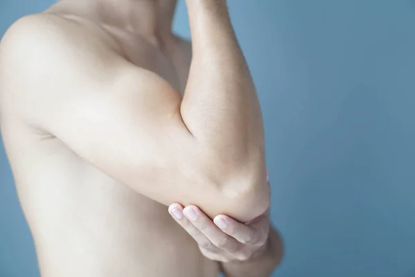 Крупним планом рука людини тримає лікоть з болем на синьому фоні, охороною здоров'я та медичною концепцією — стокове фото