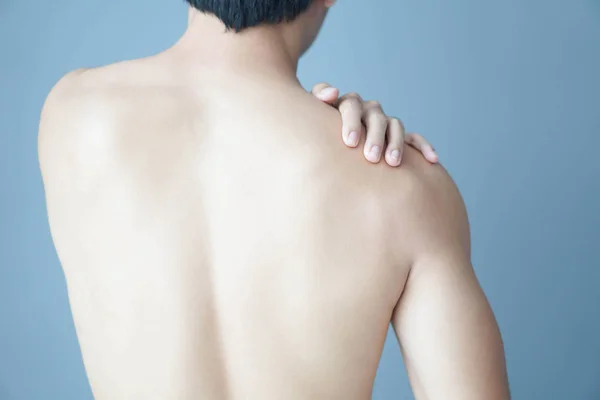 Closeup mão homem segurando ombro com dor no fundo azul, cuidados de saúde e conceito médico — Fotografia de Stock