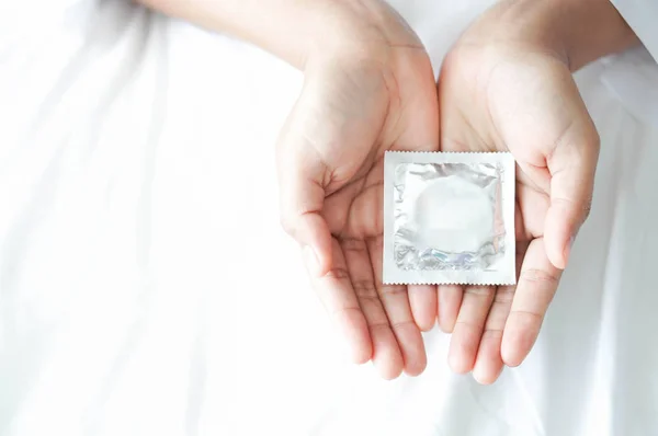 Close up mão mulher segurando preservativo deitado na cama branca, cuidados de saúde e conceito médico — Fotografia de Stock
