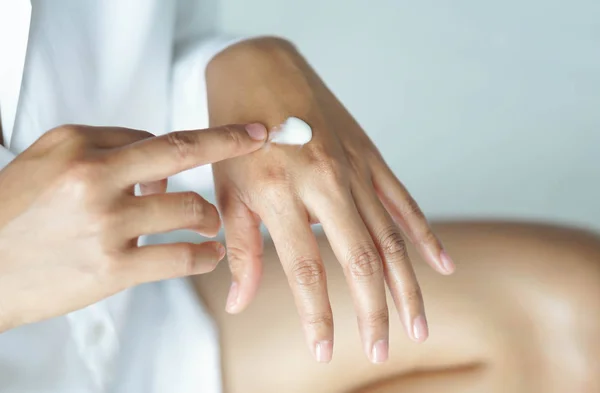 Ręka kobieta stosując krem lub balsam na rękę leżącego na białym łóżku, selektywne skupienie — Zdjęcie stockowe