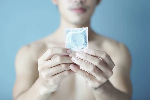 Close up homem mão segurando preservativo com fundo azul, cuidados de saúde e conceito médico, foco seletivo — Fotografia de Stock