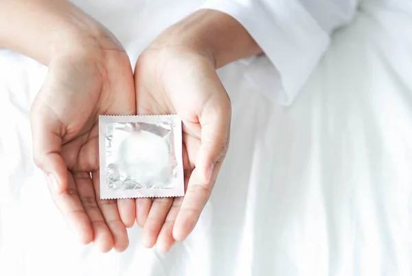Крупним планом жінка тримає презерватив лежачи на білому ліжку, охорону здоров'я та медичну концепцію — стокове фото