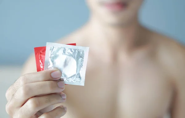 Fechar o homem mão segurando preservativo pronto para uso deitado na cama branca, cuidados de saúde e conceito médico, foco seletivo — Fotografia de Stock