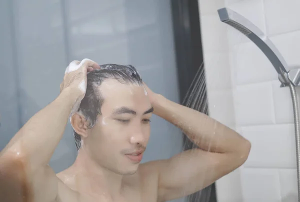 Closeup young man washing hair with with shampoo in the bathroom, vintage tone, selective focus