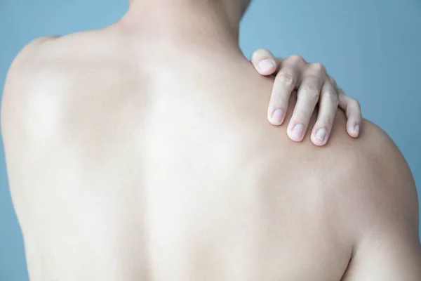 Closeup man hand holding shoulder with pain on blue background, health care and medical concept