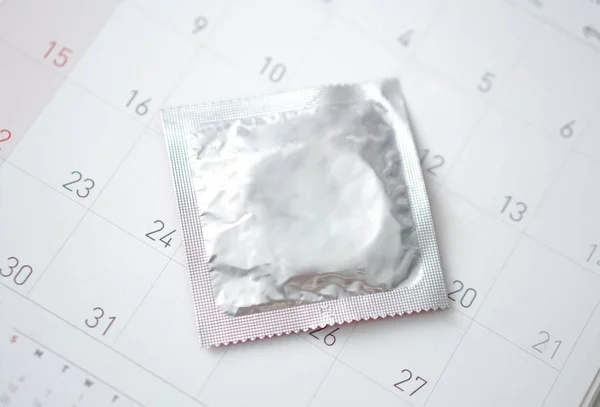 Preservativo fechado no fundo do calendário, conceito de cuidados de saúde, foco seletivo — Fotografia de Stock