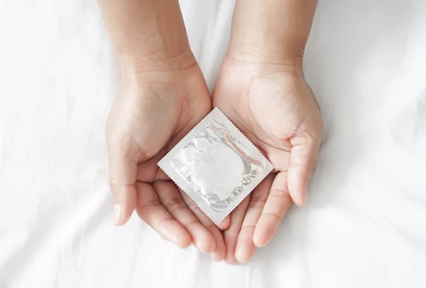 Close up mão mulher segurando preservativo deitado na cama branca, cuidados de saúde e conceito médico — Fotografia de Stock