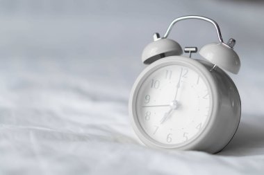 Pencereden gelen ışıkla uyanma zamanı için beyaz yatakta çalar saat, seçici odak