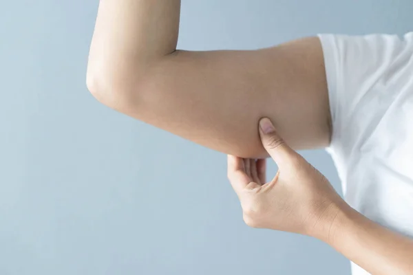 Primer plano de la mano de la mujer que comprueba la parte superior del brazo en el fondo gris cuidado de la salud y concepto médico — Foto de Stock