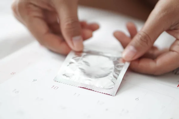 Close up mão mulher segurando preservativo no fundo do calendário, conceito de cuidados de saúde, foco seletivo — Fotografia de Stock