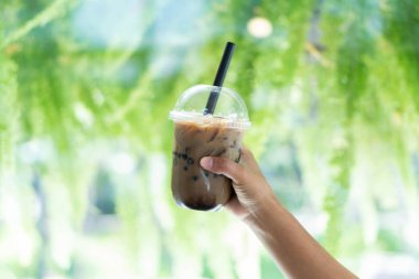 Yakın plan, elinde bir bardak buzlu kahve, baloncuklu, doğal bir arka plan.