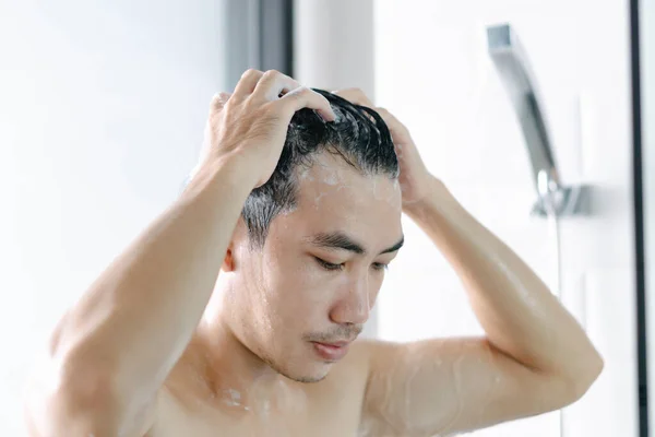 Closeup young man washing hair with with shampoo in the bathroom, vintage tone, selective focus