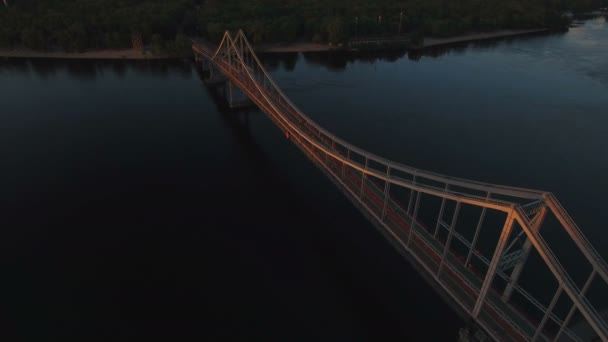 Puente peatonal sobre el río cerca de la ciudad al atardecer lanzamiento de aviones no tripulados — Vídeos de Stock