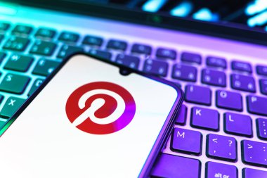 Prag, Çek Cumhuriyeti - 08 19 2025: Pinterest logosunu gösteren klavyenin üzerinde duran cep telefonunun yakından görüntüsü. Pinterest fikirleri görsel olarak keşfetmek ve kaydetmek için bir platformdur..