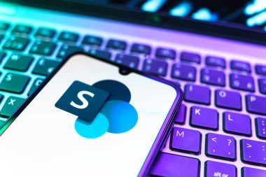 Prag, Çek Cumhuriyeti - 08 19 2025: Microsoft Sharepoint logosunu gösteren klavyenin üzerinde duran cep telefonunun yakından görüntüsü. Microsoft Sharepoint işbirliği ve belge yönetimi için bir platformdur.
