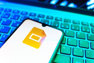 Prag, Çek Cumhuriyeti - 08 19 2025: Google Slides logosunu gösteren klavyenin üzerinde duran cep telefonunun yakından görüntüsü. Google Slides sunumlar ve slayt gösterileri oluşturmak için bir platformdur.