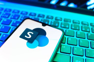 Prag, Çek Cumhuriyeti - 08 19 2025: Microsoft Sharepoint logosunu gösteren klavyenin üzerinde duran cep telefonunun yakından görüntüsü. Microsoft Sharepoint işbirliği ve belge yönetimi için bir platformdur.