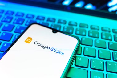 Prag, Çek Cumhuriyeti - 08 19 2025: Google Slides logosunu gösteren klavyenin üzerinde duran cep telefonunun yakından görüntüsü. Google Slides sunumlar ve slayt gösterileri oluşturmak için bir platformdur.
