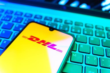 Prag, Çek Cumhuriyeti - 08 19 2025: DHL logosunu gösteren klavyenin üzerinde duran cep telefonunun yakından görüntüsü. DHL uluslararası nakliye hizmeti sunan bir lojistik şirketidir..