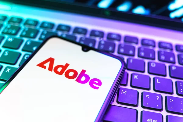 Prag, Çek Cumhuriyeti - 08 19 2025: Klavyede duran ve Adobe logosunu gösteren bir cep telefonunun yakından görüntüsü. Adobe yaratıcı araçlar ve hizmetler sunan bir yazılım şirketidir..