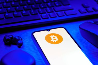 Prag, Çek Cumhuriyeti - 08 12 2025: Bitcoin logosunu gösteren klavyesi ve cep telefonu olan bir masanın yan görüntüsü. Bitcoin merkezi olmayan işlemler için dijital bir kripto para birimidir.